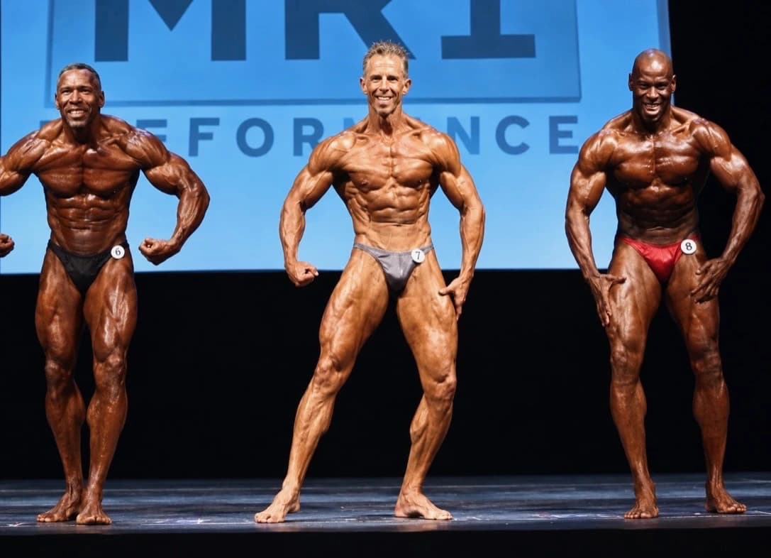 Theo Thurston (center) posing on stage in a bodybuilding lineup